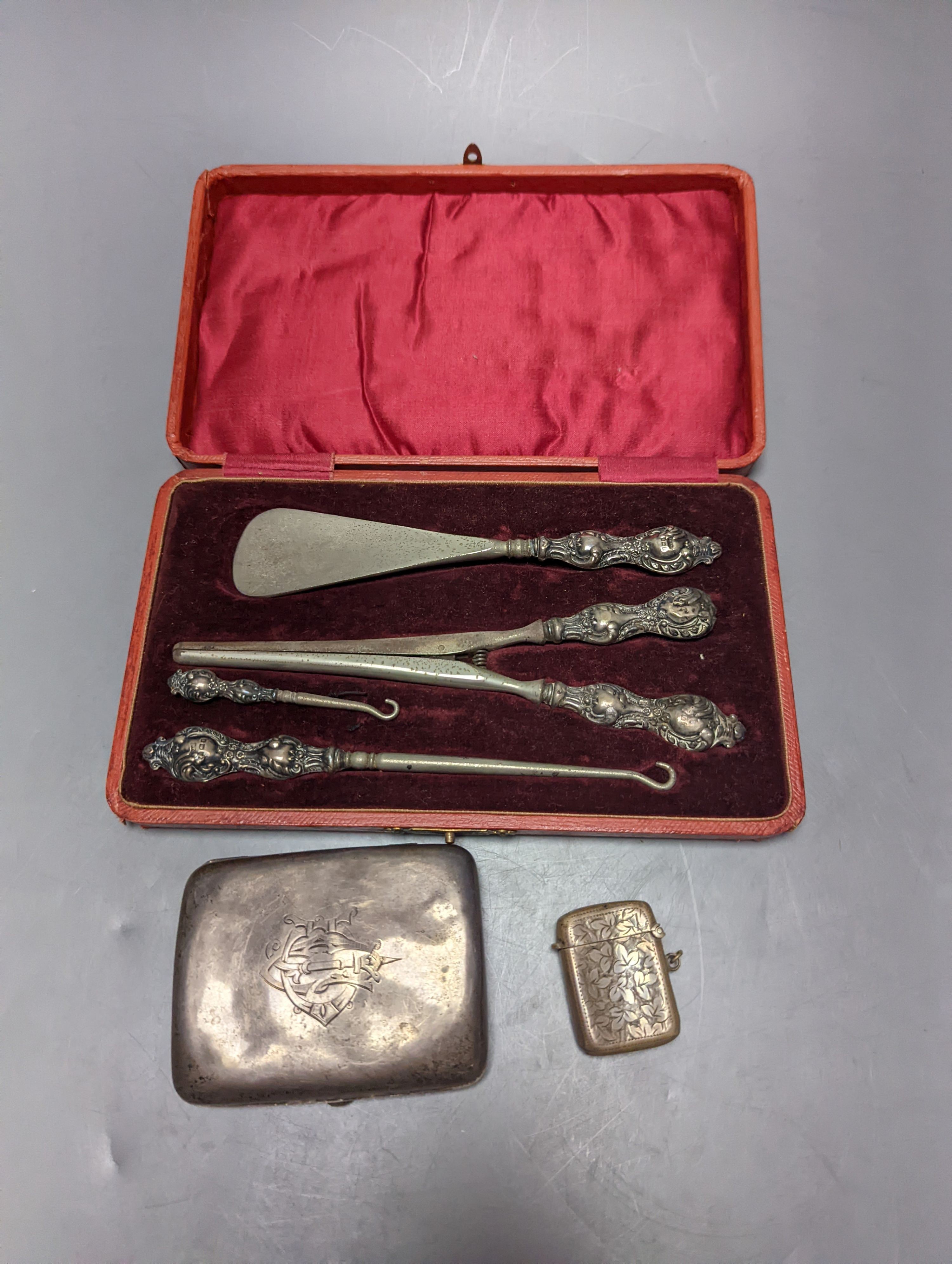 A George V silver cigarette case, an earlier silver vesta case and a cased set of button hooks, shoe horn and glove stretchers.